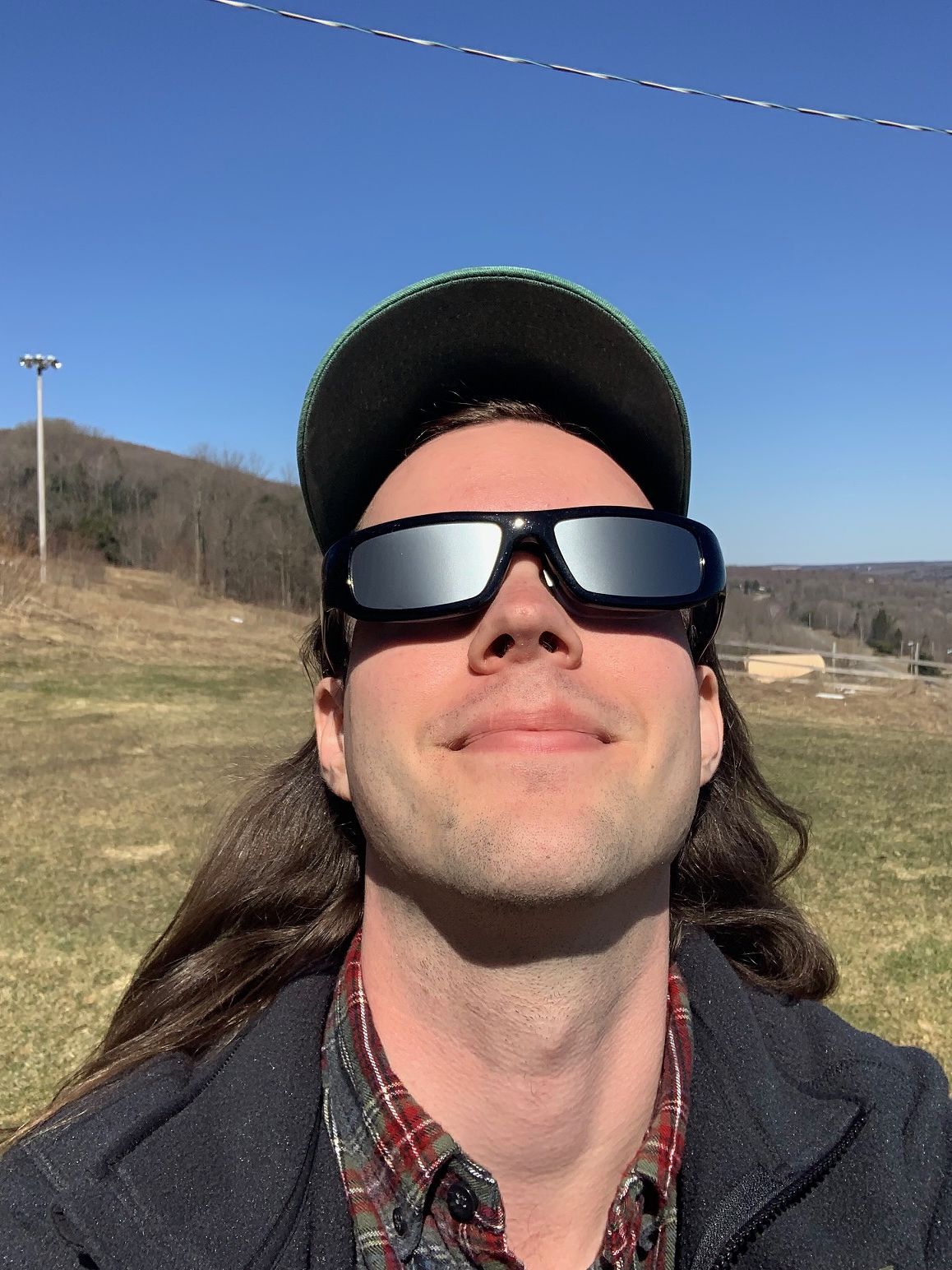 Me with eclipse glasses on a hill, looking up at the sun.